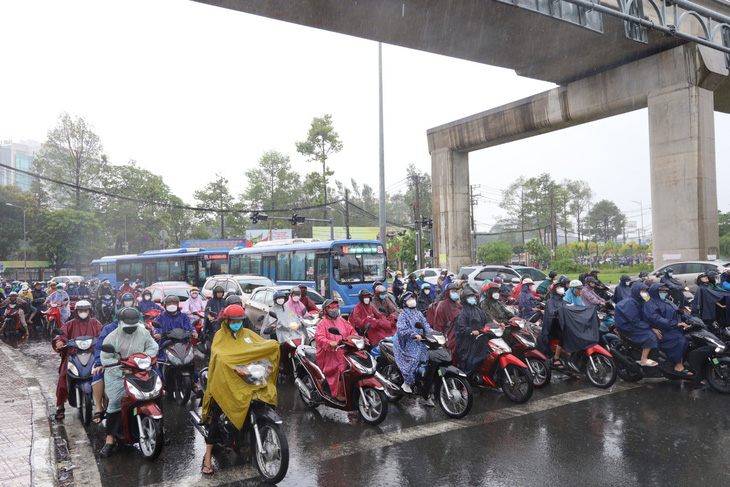 Nhiều người đứng dưới dạ cầu trú mưa khiến giao thông phía sau di chuyển chậm tại ngã tư Thủ Đức - Ảnh: NGỌC QUÝ