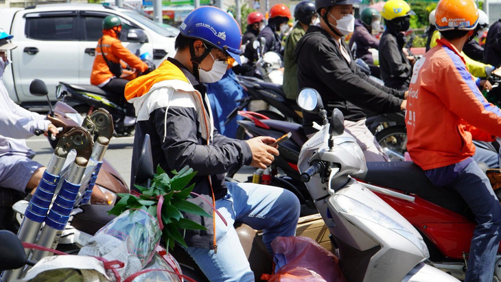 Anh thanh niên tranh thủ xem điện thoại trong lúc đợi đèn giao thông trên đường Phạm Văn Đồng, TP Thủ Đức - Ảnh: ĐỊNH DƯƠNG