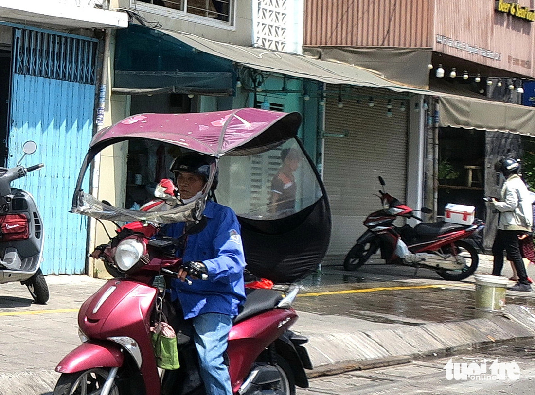 Một bác xe ôm với xe có mái che di động tự chế để tránh nắng khi đi đường