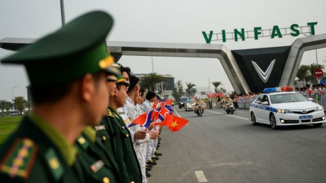 Cảnh sát Việt Nam đứng bên cạnh các sinh viên vẫy cờ Việt Nam và Triều Tiên khi đoàn xe chở đoàn Triều Tiên rời nhà máy của Vinfast tại Hải Phòng vào ngày 27/2/2019.