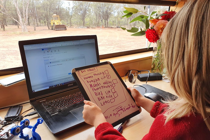 Một đứa trẻ nhìn vào chiếc bảng trắng cầm tay với chiếc máy tính xách tay trên bàn đang làm bài tập tại nhà ở vùng hẻo lánh của bang Queensland.
