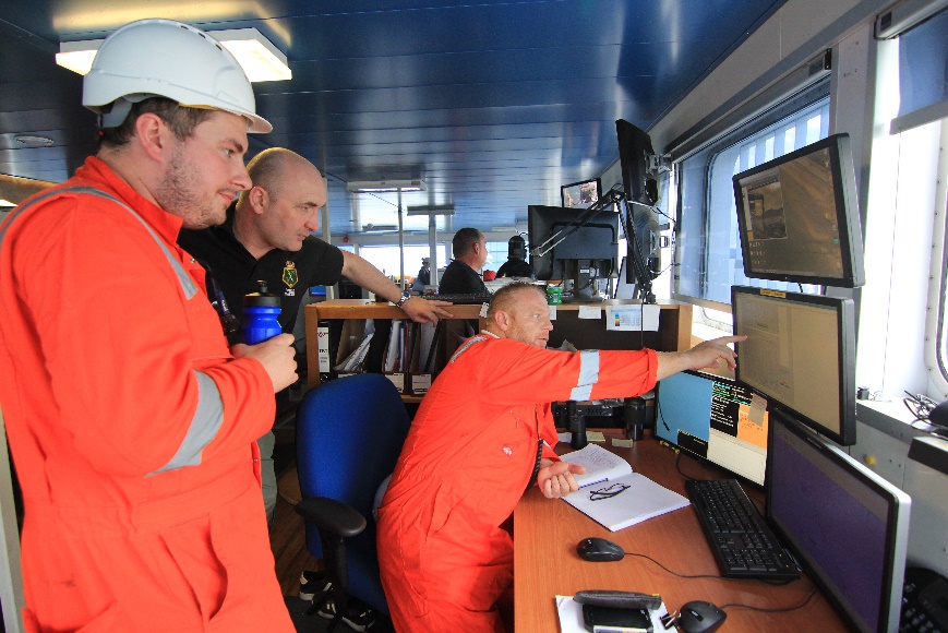 A group of men in orange jumpsuits looking at a computer screen  Description automatically generated